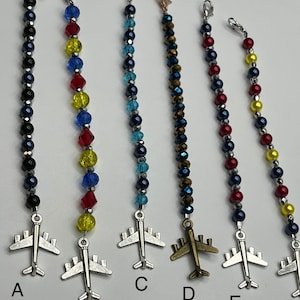 May include: A collection of beaded airplane charms in various colors. Each charm features a silver-tone airplane pendant and a string of colorful beads. The charms are attached to a silver-tone clasp.
