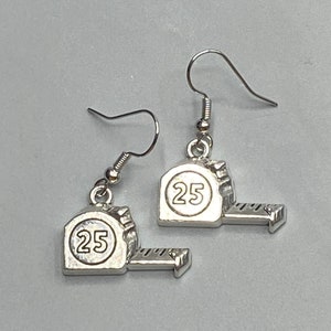May include: Silver-toned earrings featuring a tape measure design. Each earring has a small, detailed tape measure charm with the number "25" inside a circle. The earrings hang from simple fish hook ear wires.