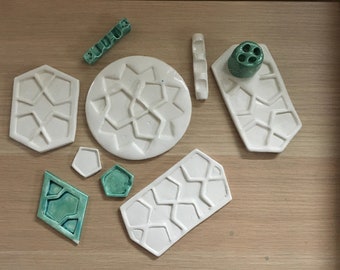 May include: A set of nine ceramic paint palettes with a geometric pattern. The palettes are in various shapes and sizes, including round, square, and rectangular. Some of the palettes are white, while others are green.
