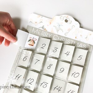 May include: A white and grey Christmas advent calendar with a floral design and the text "Merry Christmas". The calendar has 15 numbered squares, each with a small flap that can be opened to reveal a surprise.