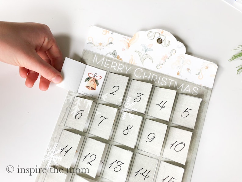 May include: A white and grey Christmas advent calendar with a floral design and the text "Merry Christmas". The calendar has 15 numbered squares, each with a small flap that can be opened to reveal a surprise.