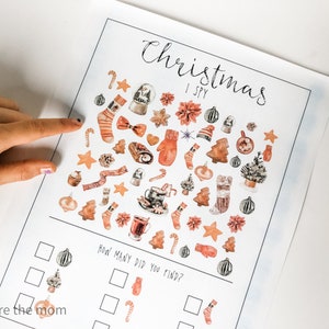 May include: A printable Christmas I Spy game with a white background and illustrations of various Christmas items in shades of brown, orange, and red. The items include ornaments, candy canes, mittens, stockings, and Christmas trees. The text "Christmas I Spy" is written in black cursive at the top of the page. Below the illustrations is a section with boxes for counting how many of each item you can find.