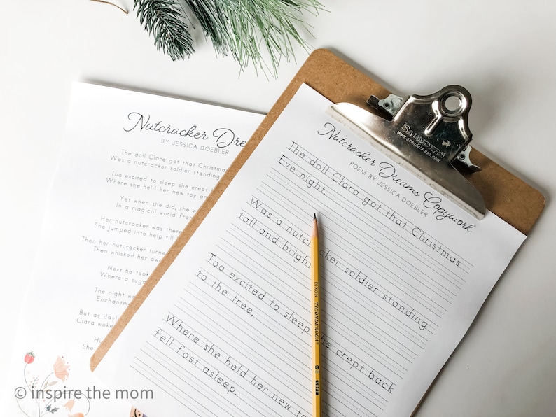Op de afbeelding: Een afdrukbaar gedicht met de titel "Nutcracker Dreams Copywork" van Jessica Doebler. Het gedicht staat op een wit vel papier met lijnen en ligt op een klembord met een bruine achterkant. Het gedicht gaat over een pop genaamd Clara die een notenkraker-soldaat krijgt voor Kerstmis. Het gedicht is geschreven in cursief.