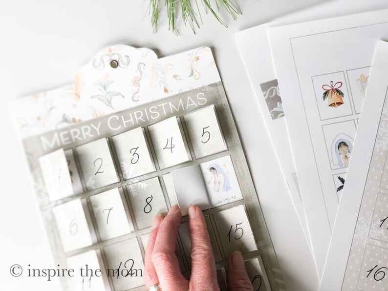 May include: A white and grey advent calendar with the words "Merry Christmas" printed on the top. The calendar has 24 numbered squares, each with a small window that can be opened to reveal a surprise. The calendar is decorated with a floral pattern.