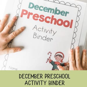 May include: A white activity binder for December Preschool, with the title in red and teal. The cover features a cartoon elf holding a candy cane. The binder is held by two hands.