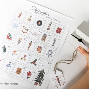 Op de afbeelding: Een printbare Notenkraker-Adventskalender met 24 genummerde vakjes, elk met een andere kerstthema-illustratie. De kalender is gedrukt op wit papier en heeft een eenvoudig, minimalistisch ontwerp.
