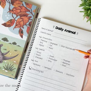 May include: A spiral-bound Daily Animal worksheet featuring sections for name, scientific name, classification, habitat, diet, and interesting facts, positioned next to an open illustrated book showing a rhinoceros and leaf fish.