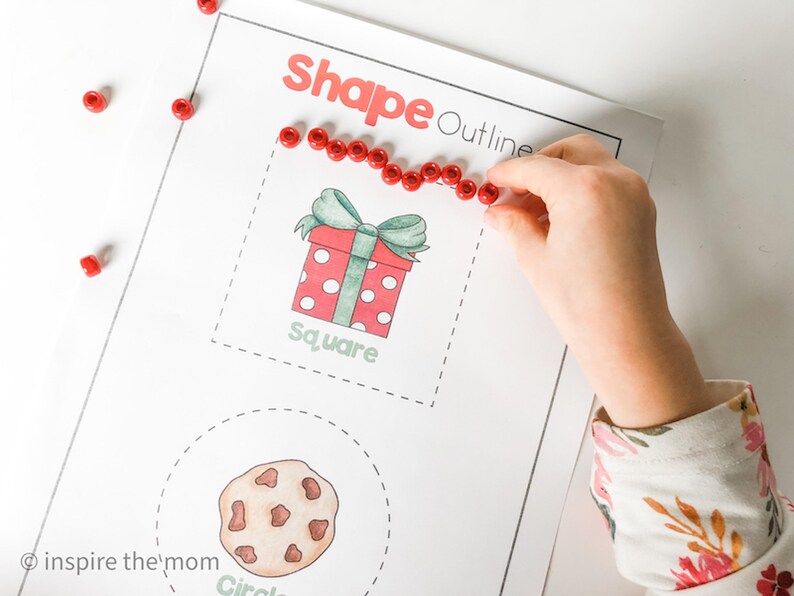 May include: A worksheet with the words "Shape Outline" in red. A hand is placing red beads around a square-shaped gift box illustration. The word "square" is below the gift box. A cookie illustration is below the gift box.