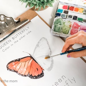 Pode incluir: Uma prancheta com uma ilustra&ccedil;&atilde;o de borboleta monarca para colorir. A borboleta est&aacute; parcialmente colorida em laranja e preto. Uma paleta de aquarela e um pincel tamb&eacute;m s&atilde;o vis&iacute;veis.