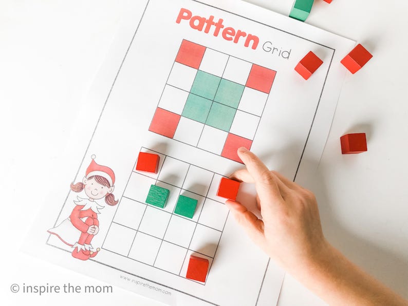 May include: A printed "Pattern Grid" worksheet with red and green squares, and a cartoon elf illustration. A hand places a red block on the grid. Several red and green blocks are scattered around the worksheet.