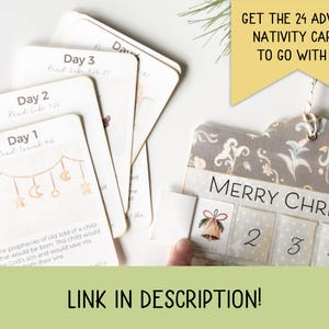 May include: A Christmas advent calendar with a grey and white floral pattern. The calendar has 24 numbered windows, and the text "Merry Christmas" is printed on the front. The calendar is decorated with a small bell.