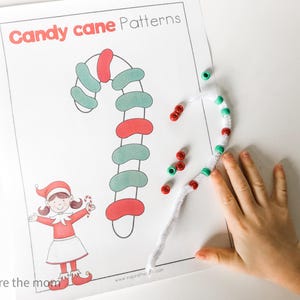 May include: A printed sheet with "Candy cane Patterns" in red text. A drawn candy cane is colored red and green. A child's hand is next to a pipe cleaner candy cane with red and green beads. A cartoon elf is also on the sheet.