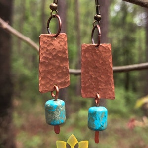 May include: A pair of copper earrings with turquoise beads. The copper is hammered and has a rustic look. The earrings are hanging from a branch.