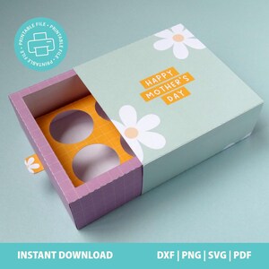 May include: A rectangular sliding gift box with a light green sleeve featuring white daisy illustrations and the text HAPPY MOTHER'S DAY in orange. The inner tray is purple with a white grid pattern and contains a yellow insert with four circular cutouts.