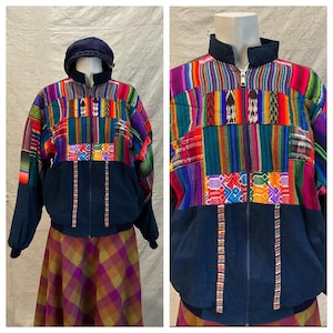 Puede incluir: Una colorida chaqueta con cremallera y patchwork con base y capucha azul marino. La chaqueta presenta rayas vibrantes y patrones geométricos en rojo, verde, morado y naranja. La chaqueta se exhibe en un maniquí.