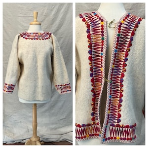 Puede incluir: Conjunto de jersey y chaqueta de lana color crema con detalles bordados coloridos. El jersey tiene cuello redondo y mangas largas con puños bordados. La chaqueta presenta un ribete decorativo y un cierre de gancho. El bordado incluye rojo, amarillo, azul y verde.