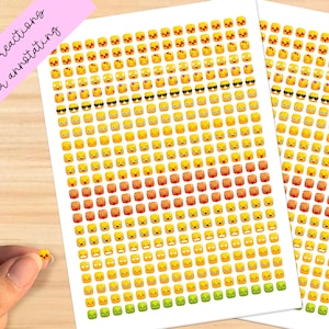 May include: Sheets of emoji stickers featuring various facial expressions in yellow, orange, and green. Some emojis have sunglasses. Text on a pink label reads "emoji reactions for annotating". A hand holds a single sticker.