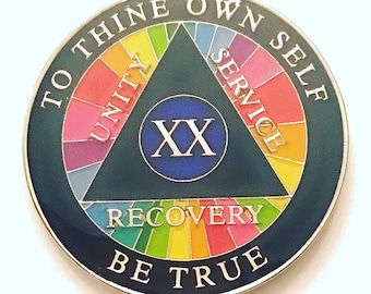 May include: A silver coin with a black background and a rainbow circle around the edge. The center of the coin features a blue circle with the Roman numeral XX inside. The triangle inside the circle has the words "Unity", "Service", and "Recovery" inscribed on each side. The words "To Thine Own Self Be True" are inscribed around the outer edge of the coin.