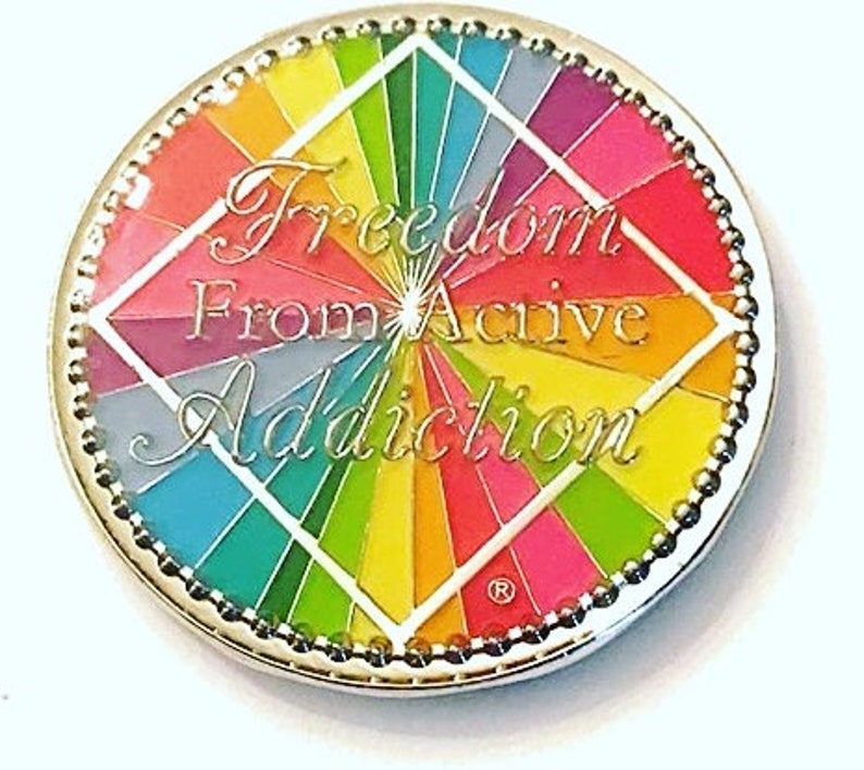 May include: A silver-colored round pin with a rainbow design and the text "Freedom From Active Addiction".