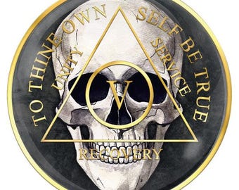 May include: A gold coin with a black and white skull illustration in the center. The skull is surrounded by a triangle with the words "To thine own self be true" and "Unity, Service, Recovery" inscribed around the triangle.
