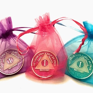 May include: Three 1-year sobriety coins in purple, pink, and teal organza bags. Each coin features a triangle with the words "To Thine Own" at the top, "Unity" on the left, "Service" on the right, "Self Be True" at the bottom, and "Recovery" in the center.