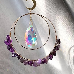 May include: A decorative suncatcher featuring a gold-colored crescent moon and two concentric gold hoops. The lower hoop is adorned with amethyst stones. A large, iridescent crystal prism hangs from the center, reflecting a rainbow of colors.