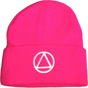 May include: A bright pink beanie hat with a white embroidered triangle within a circle. The hat is made of a knitted material and has a folded brim. The design is simple and modern.
