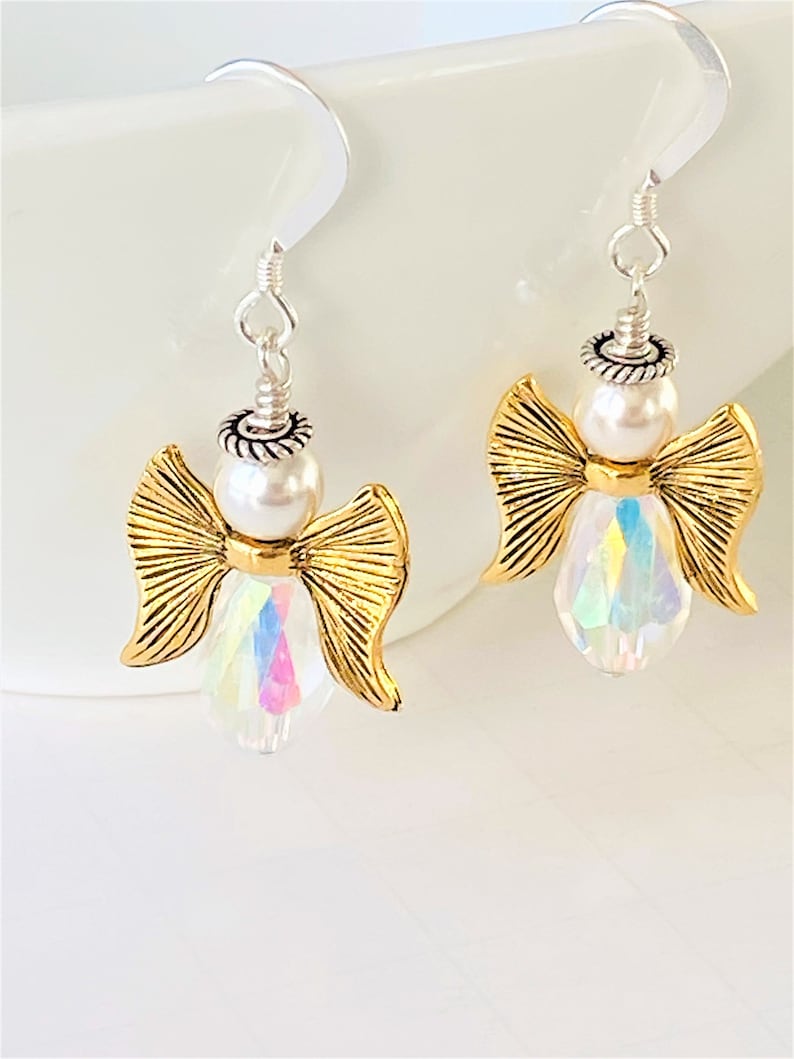 May include: Gold angel dangle earrings with iridescent crystal and white pearl accents.