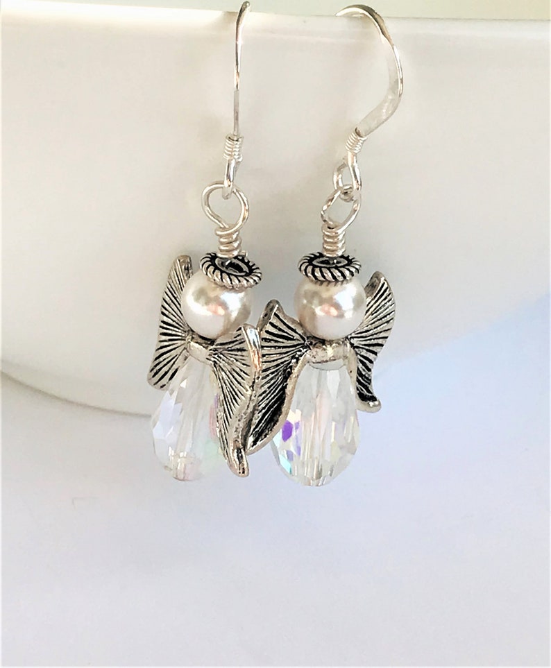 May include: Silver angel dangle earrings with a white pearl and clear crystal bead.