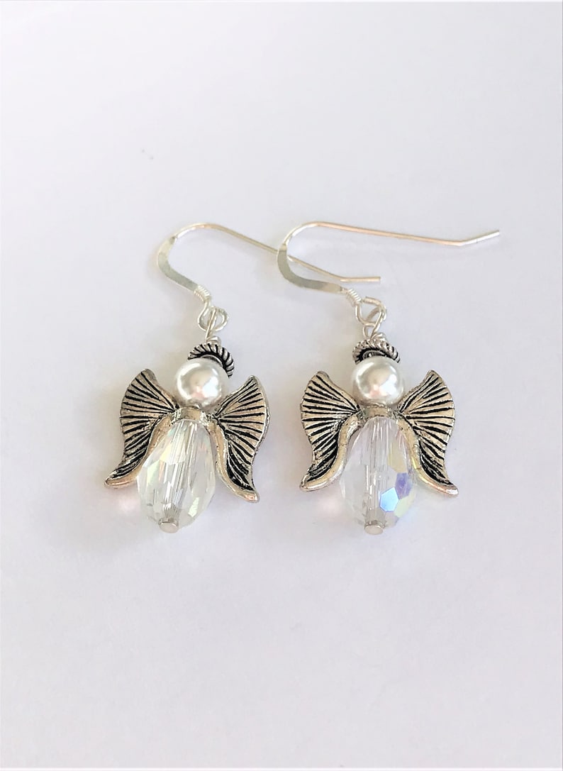 May include: A pair of silver angel dangle earrings with clear crystal beads. The angels have silver wings and a pearl head.