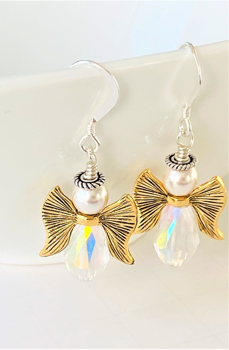 May include: A pair of silver dangle earrings featuring a gold angel with a pearl and iridescent crystal accents.