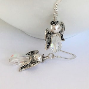 May include: A pair of silver angel earrings with clear crystal accents and white pearl beads.