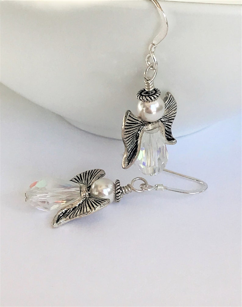 May include: A pair of silver angel earrings with clear crystal accents and white pearl beads.