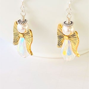 May include: A pair of gold angel dangle earrings with iridescent crystal accents and white pearl beads.