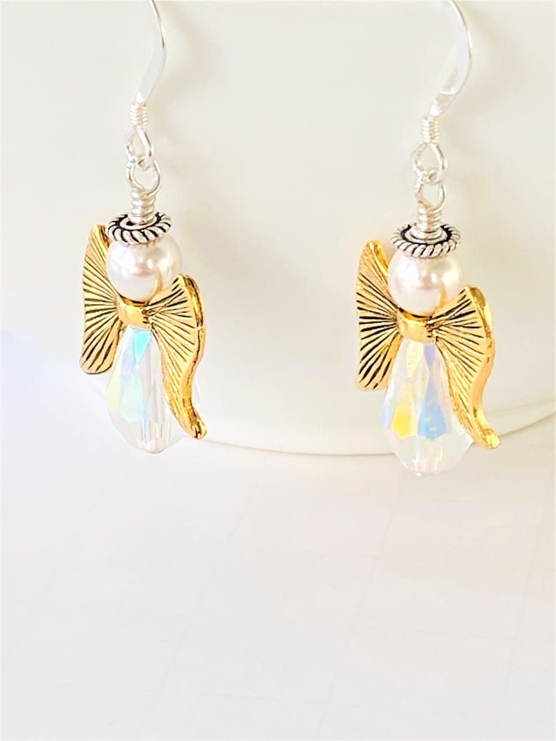 May include: A pair of gold angel dangle earrings with iridescent crystal accents and white pearl beads.