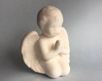 Może przedstawiać: Biała ceramiczna figurka anioła z skrzydłami, klęcząca z dłońmi złożonymi do modlitwy.