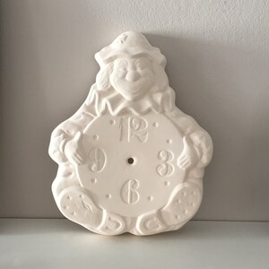 Może przedstawiać: Biały ceramiczny zegar w kształcie klauna trzymający tarczę zegara z cyframi rzymskimi.