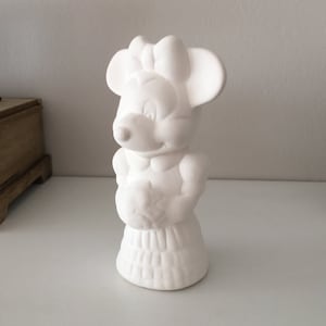 May include: White ceramic figurine of a cartoon mouse with a bow. The mouse is wearing a dress and holding a flower.