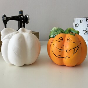 Könnte beinhalten: Zwei Keramik-Kürbisse, einer weiß und einer orange mit einem bemalten schwarzen lächelnden Gesicht.