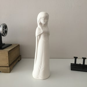 Puede incluir: Figurilla de cerámica blanca de una mujer con un vestido largo y las manos juntas en oración.