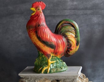 Peut inclure: Une figurine de coq rouge, jaune et verte avec un design détaillé. Le coq est debout sur une base verte avec des feuilles.