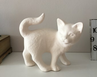 May include: White ceramic cat figurine with a curled tail. The cat is standing on all four paws and has a playful expression.