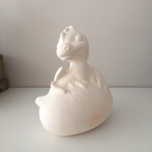 May include: White ceramic dragon figurine with a textured surface. The dragon is curled up in a ball with its head raised and its eyes closed.