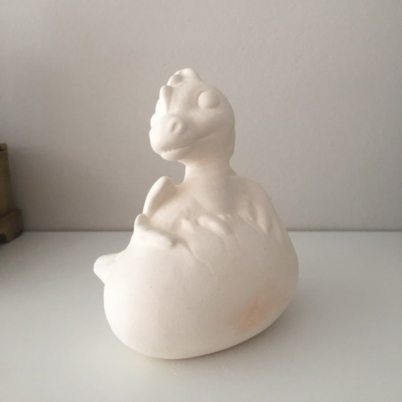 May include: White ceramic dragon figurine with a textured surface. The dragon is curled up in a ball with its head raised and its eyes closed.