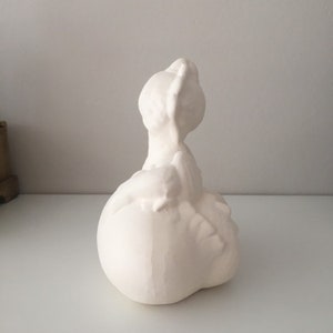 May include: White ceramic sculpture of a woman with her head tilted back and her arms raised above her head. The sculpture is in a seated position and has a smooth, matte finish.