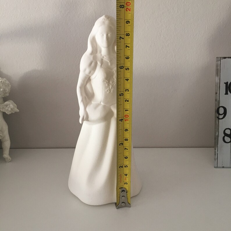 May include: White ceramic figurine of a woman in a long dress holding a bouquet of flowers. The figurine is 19 inches tall.