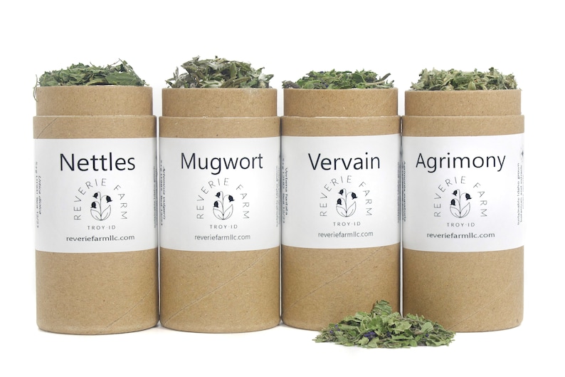 May include: Four brown cardboard tubes with white labels containing dried herbs. The labels read "Nettles", "Mugwort", "Vervain", and "Agrimony". Each label also includes the text "Reverie Farm" and a website address.