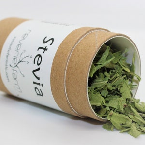 May include: A brown cardboard tube with a white label that says "Stevia" and "Reverie Farm" with a small plant graphic. The tube is open and green dried stevia leaves are spilling out.