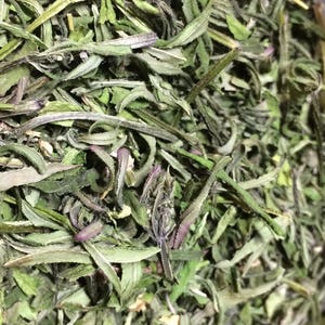 May include: Close-up of a pile of dried green leafy herbs. The herbs are finely chopped and have a light green color.