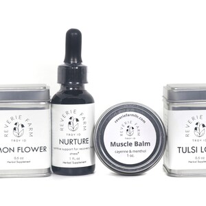 May include: Four silver tins with white labels containing herbal supplements. The labels feature the brand name "Reverie Farm" and the product names "Lemon Flower", "Nurture", "Muscle Balm", and "Tulsi Love". A dark glass bottle with a dropper is also included, labeled "Nurture".